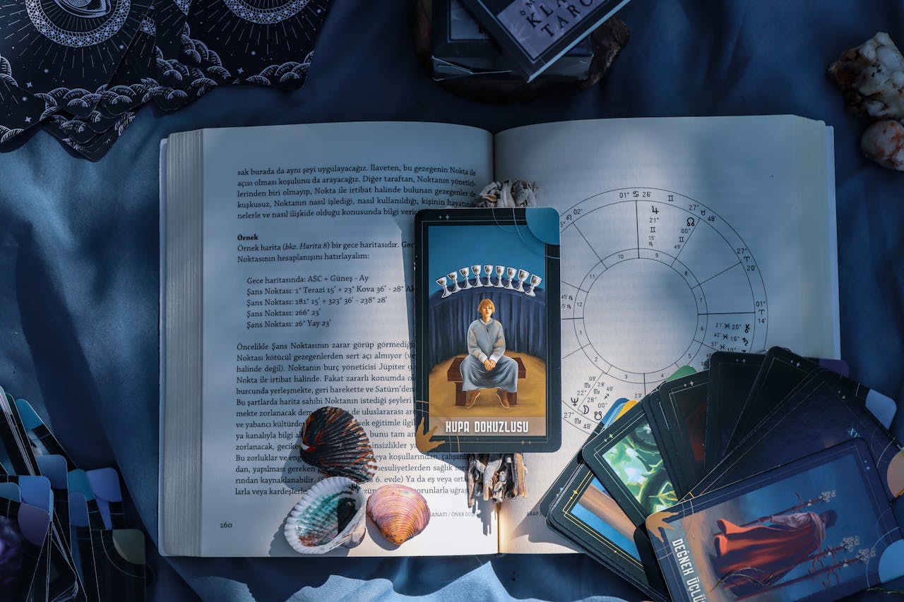 An artistic flat lay of tarot cards and astrology on a book with seashells, featuring Kupa Dokuzlusu card.
